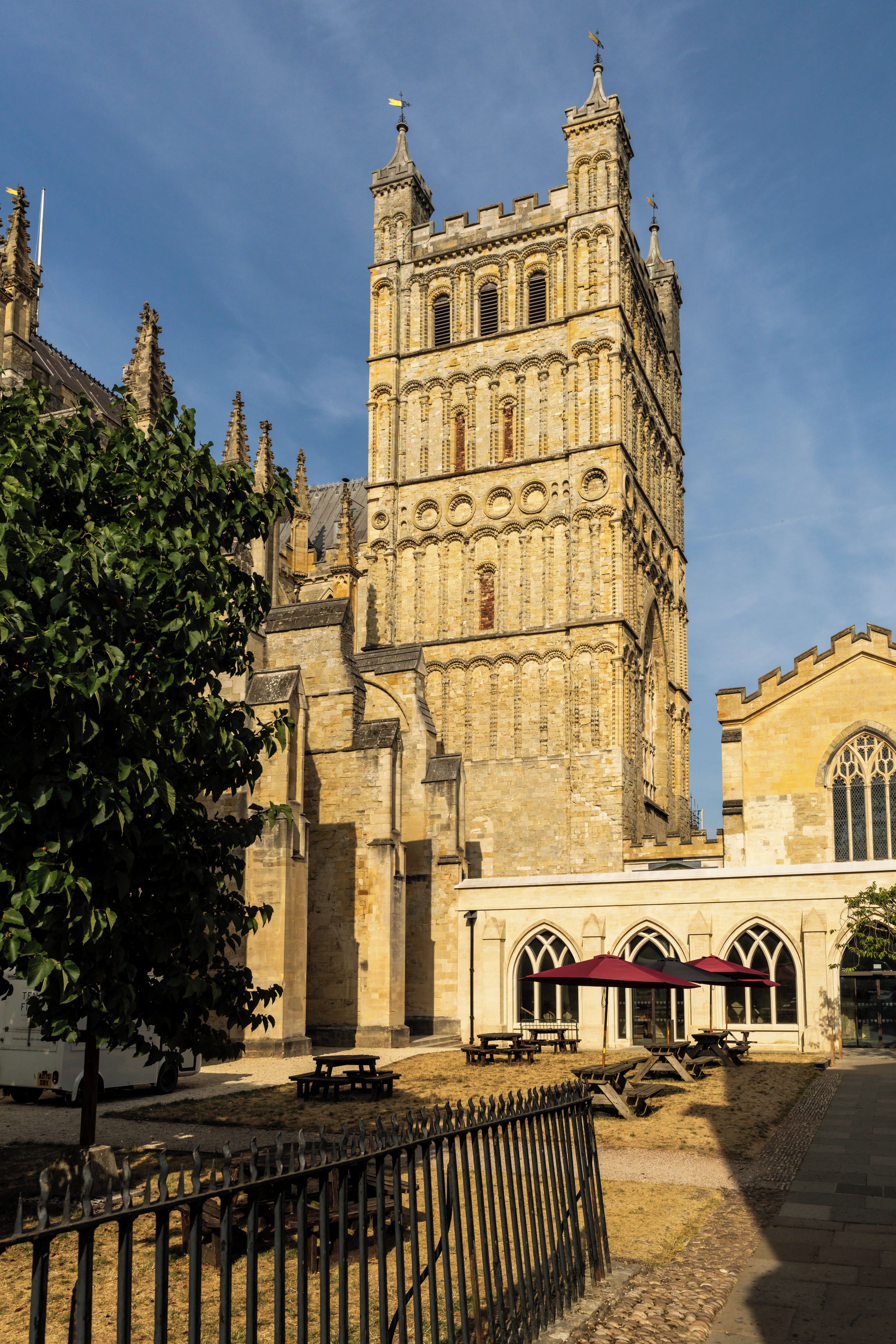 A historic building with a prominent tower and a smaller adjacent structure with tables and umbrellas.