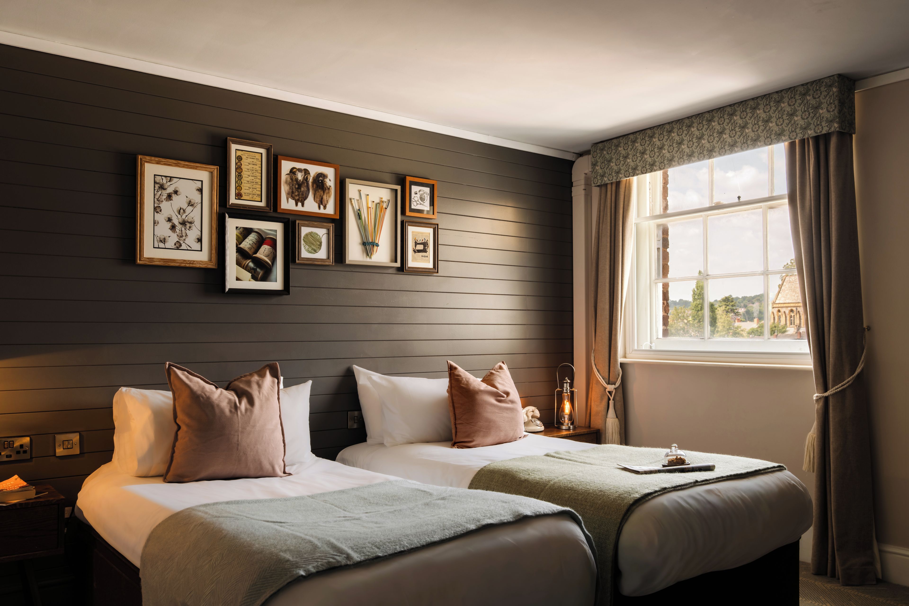 A hotel room with two beds, a window with curtains, and a wall with framed pictures.