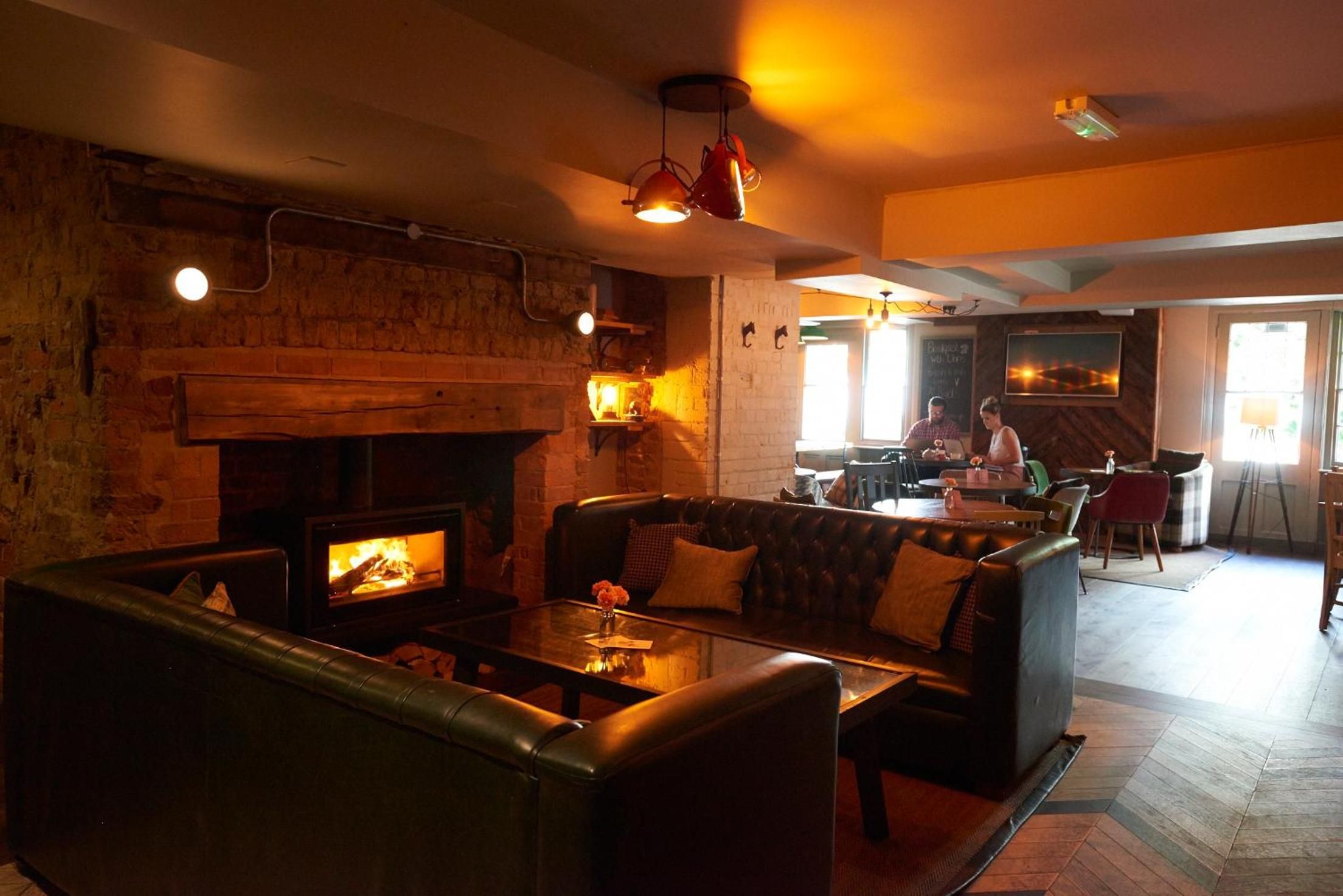 A cozy lounge area with a fireplace, leather seating, and a bar in the background.