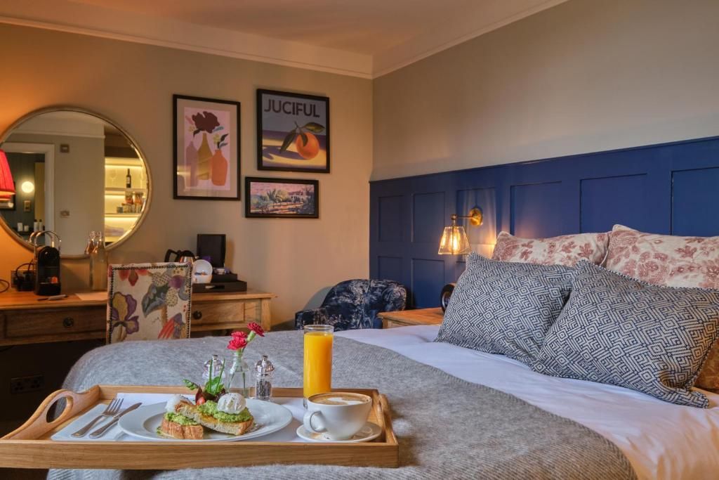 A hotel room with a bed, a bedside table, a tray with breakfast items, and artwork on the wall.