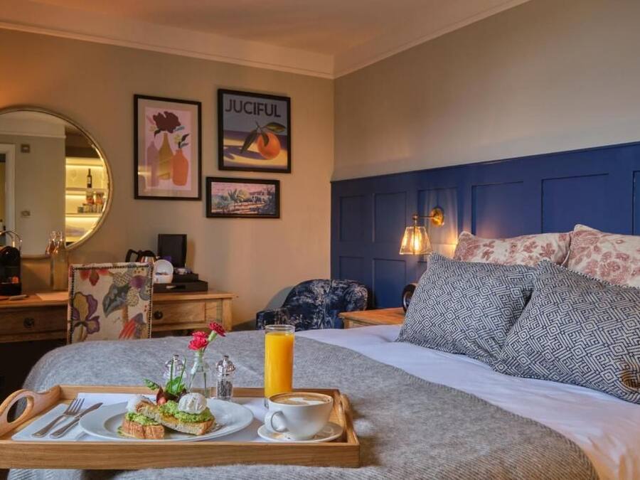 A hotel room with a bed, a bedside table, a tray with breakfast items, and artwork on the wall.