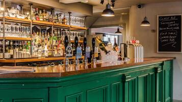 Un espace bar avec un comptoir vert, diverses bouteilles, des verres et un menu écrit à la craie sur un tableau noir.