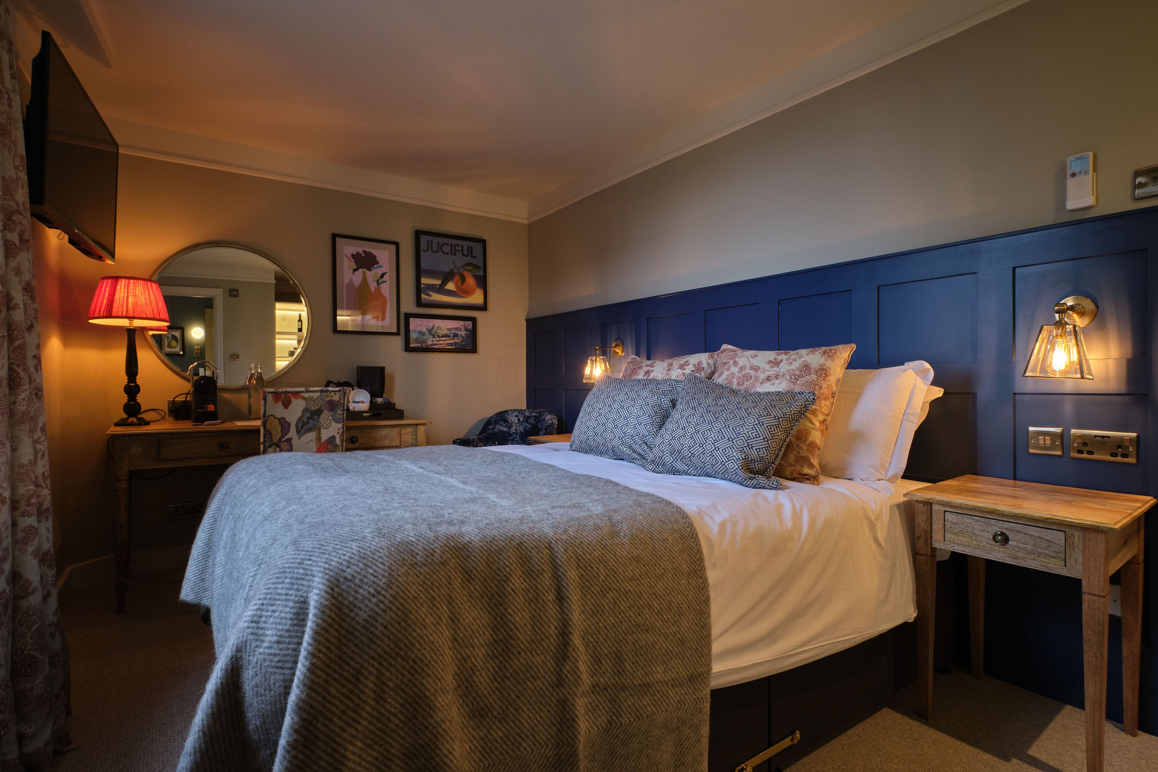 A neatly arranged bedroom with a bed, bedside tables, a lamp, a mirror, and wall-mounted light fixtures.