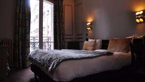 Una camera d'albergo con un letto grande, due lampade ai comodini, una finestra con tende e un termosifone.