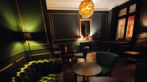 Un'area lounge scarsamente illuminata, con un divano in pelle imbottita, poltrone verdi e un tavolino rotondo.
