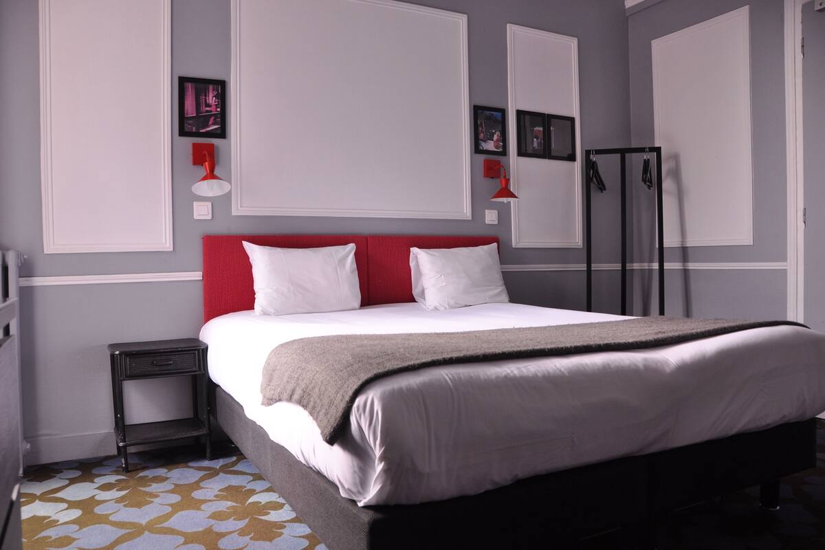 A neatly made bed with white and red bedding, a small bedside table, and a patterned rug.