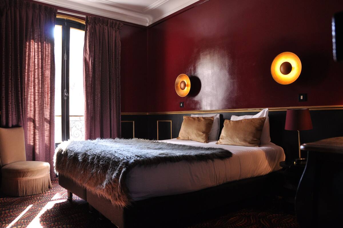 A hotel room with a large bed, two wall sconces, a chair, and a small table.