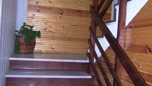 Una escalera de madera con barandilla que lleva a un rellano con una cesta que contiene plantas verdes.