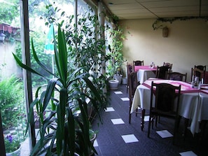 A dining area with tables and chairs, potted plants, and a view of greenery outside. - Guest House Zodiac (Samokov)
