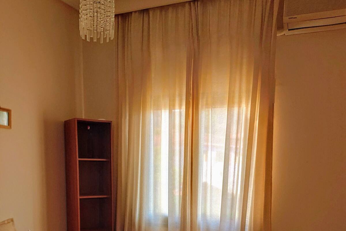A hotel room with a red bed, a wooden wardrobe, a small desk, and a window with curtains.