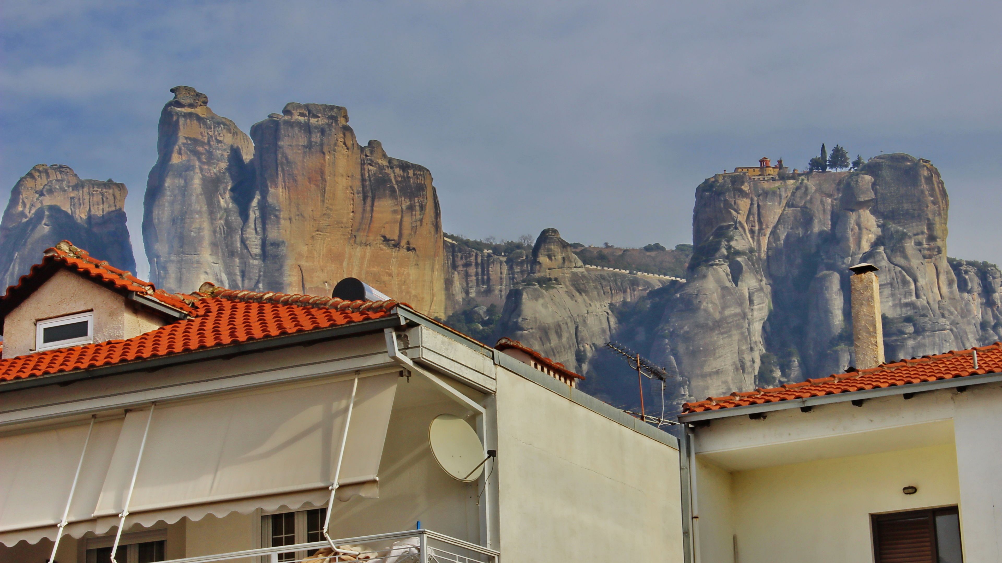 A building with a red-tiled roof and a satellite dish. In the background, there are tall, rocky cliffs.