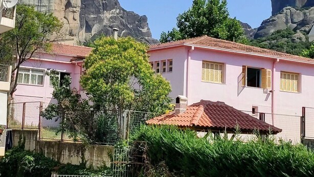 A residential area with pink houses, a large rock formation, and a clear blue sky. - King Lodge (Kalabaka)