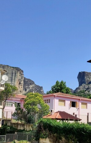 A residential area with pink houses, a large rock formation, and a clear blue sky. - King Lodge (Kalabaka)