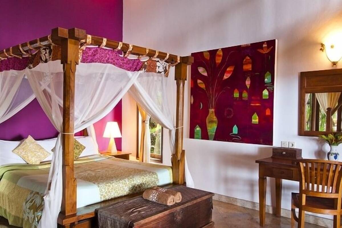 Una cama con dosel, un escritorio y una silla en una habitación con paredes moradas y un cuadro abstracto grande.