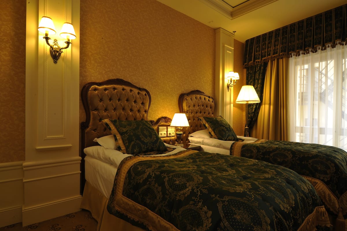 A hotel room with two beds, a nightstand, and wall sconces.