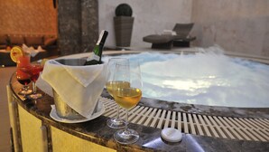 A hot tub with two glasses of wine and a bottle of champagne on a marble countertop.