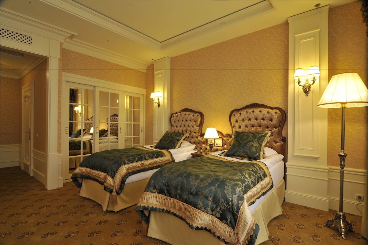 A hotel room with two large beds, a sitting area with a chair and a table, and a wardrobe with glass doors.