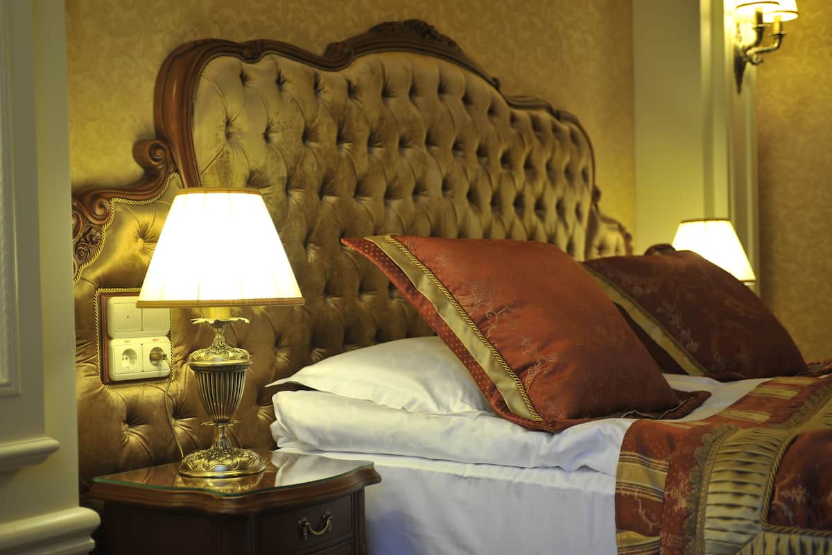 A bedroom with a tufted headboard, a bedside table with a lamp, and a bed with white linens and red pillows.