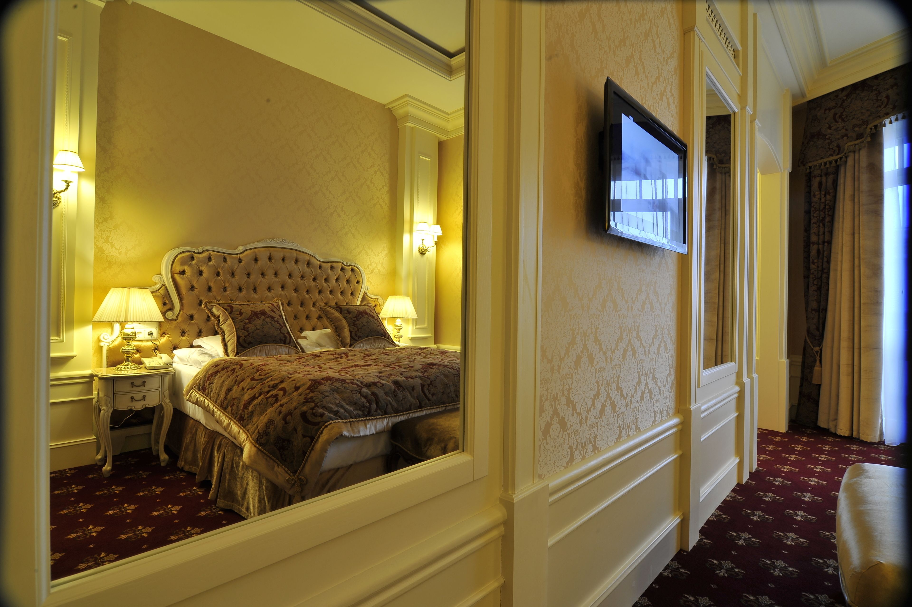 Habitación de hotel con una cama grande, un televisor montado en la pared y un espejo que refleja la habitación.