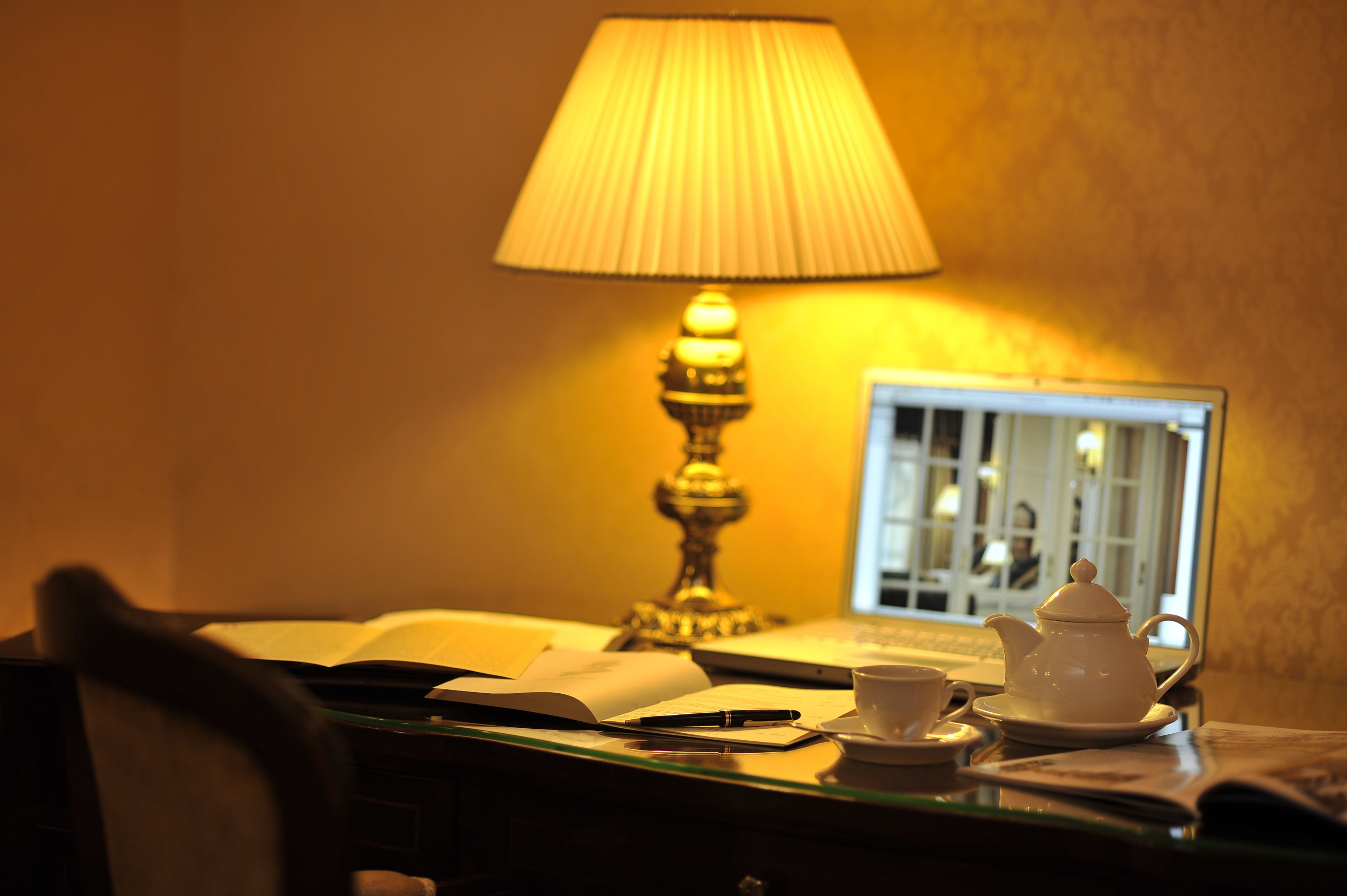 A desk with a laptop, a teapot, a cup, and an open book.