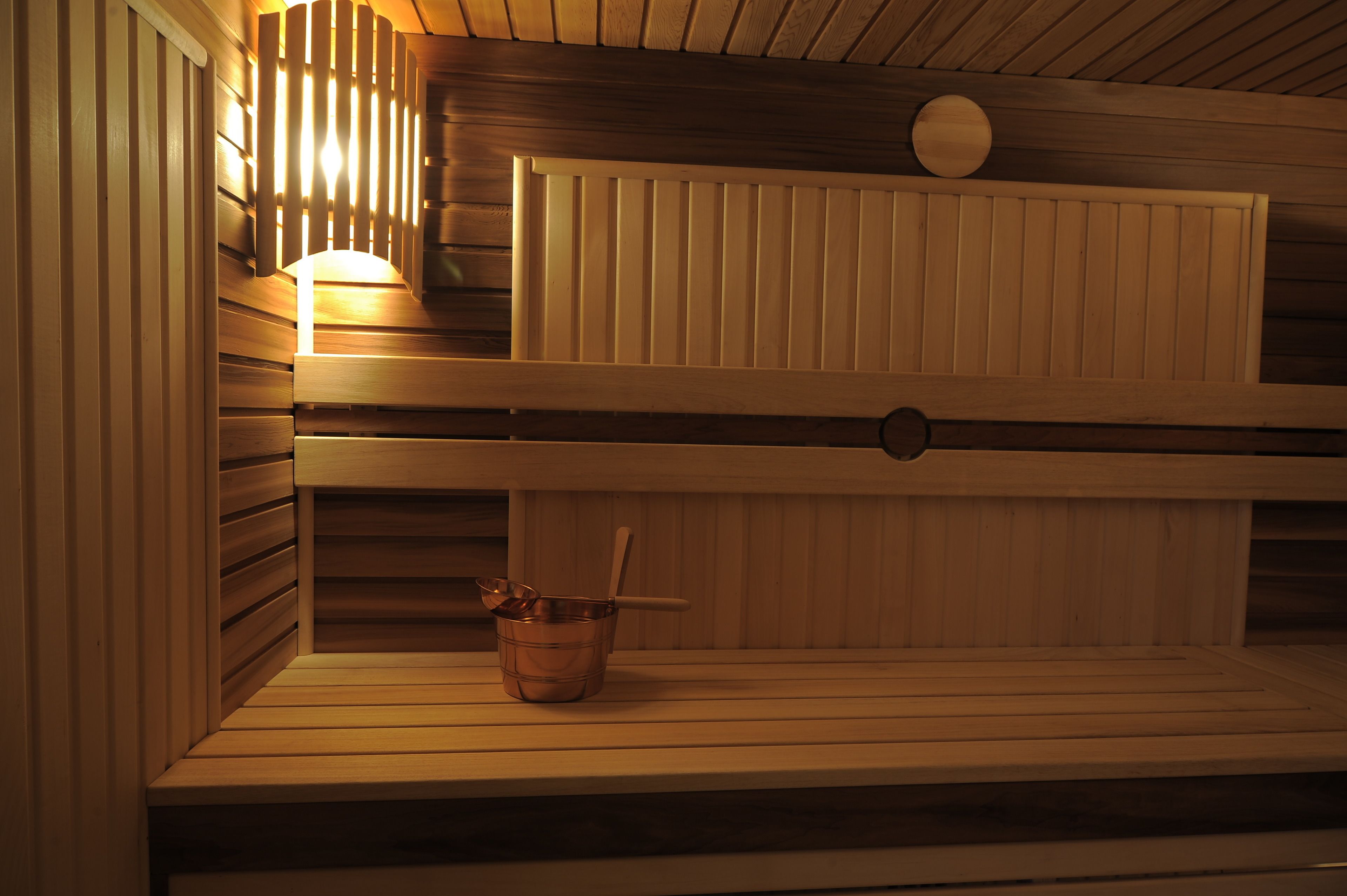 A sauna with wooden benches and a metal bucket.