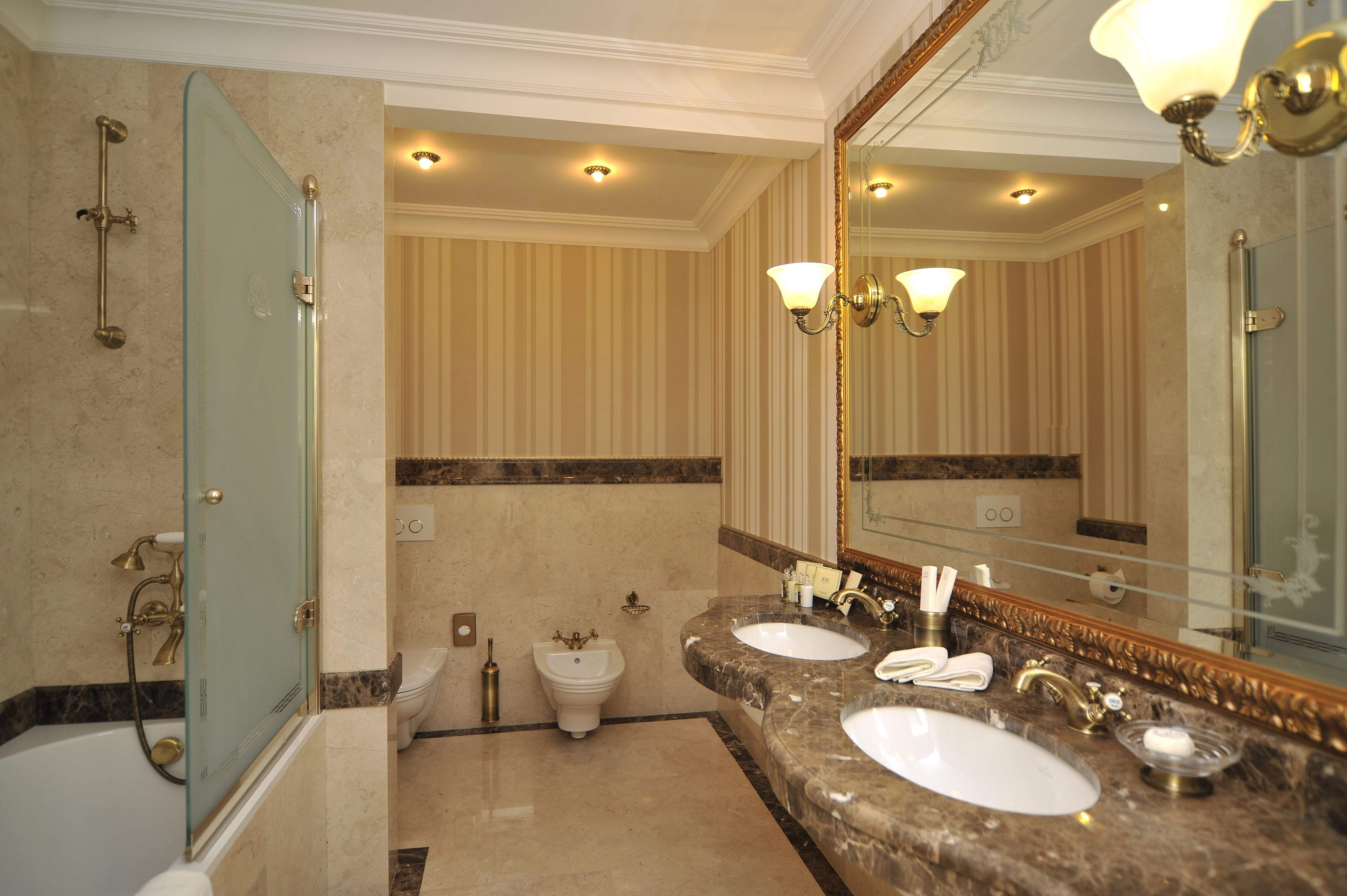Un bagno di lusso con due lavabi, box doccia in vetro e uno specchio grande con cornice dorata.