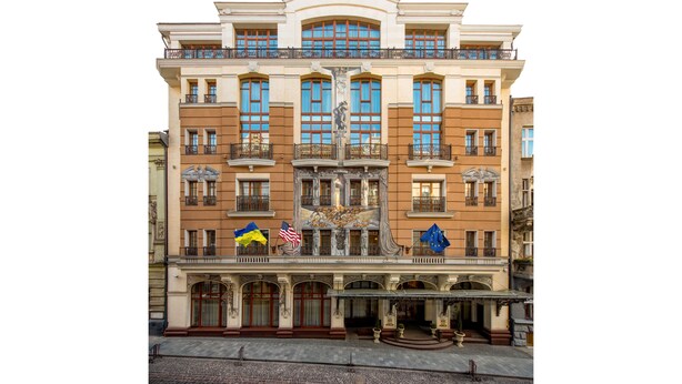 A historic building with a central fountain, ornate balconies, and flags.
