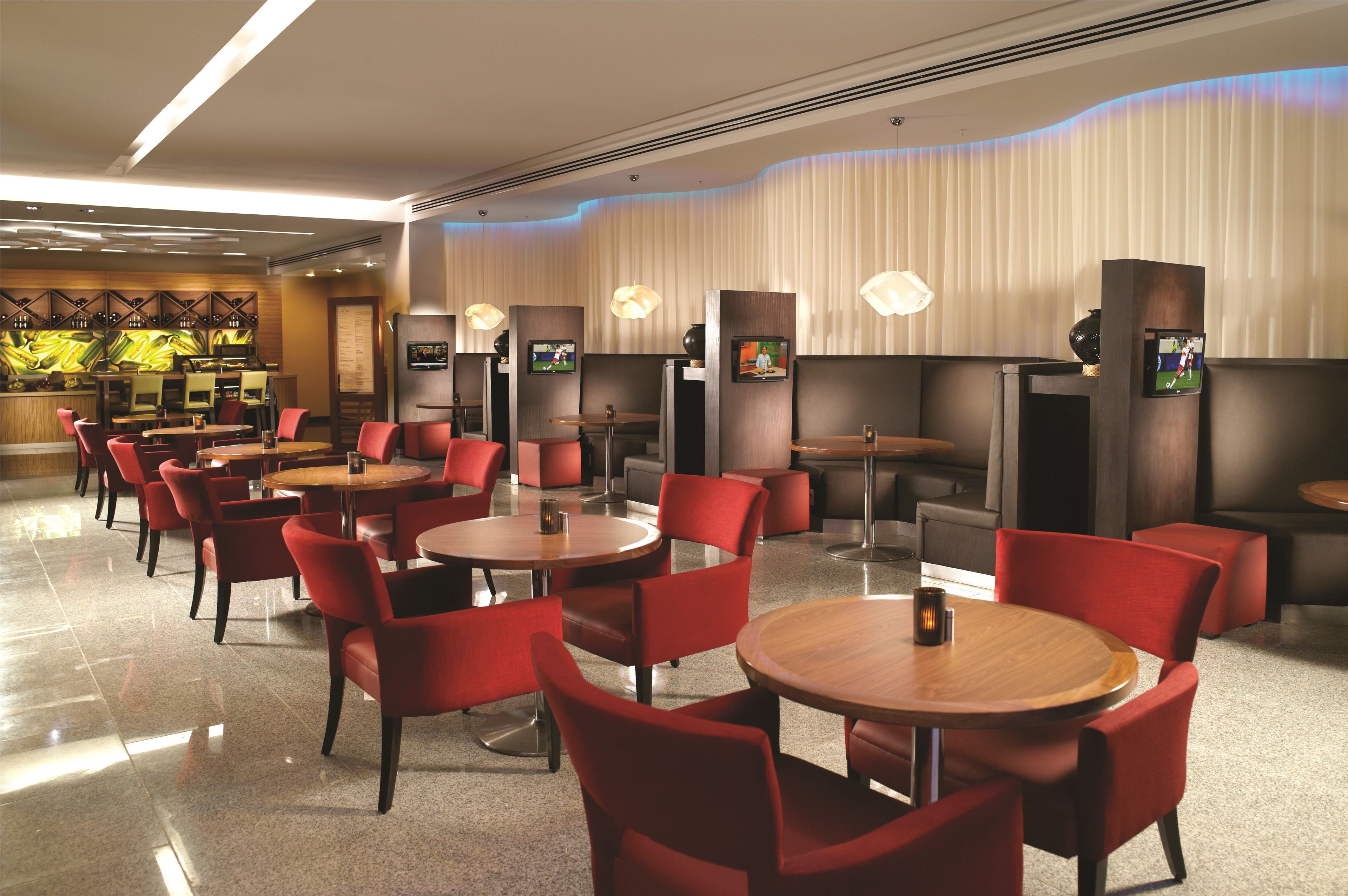 En moderne restaurant med røde polstrede stole og runde borde, med indbygget belysning og et slebet flisegulv.