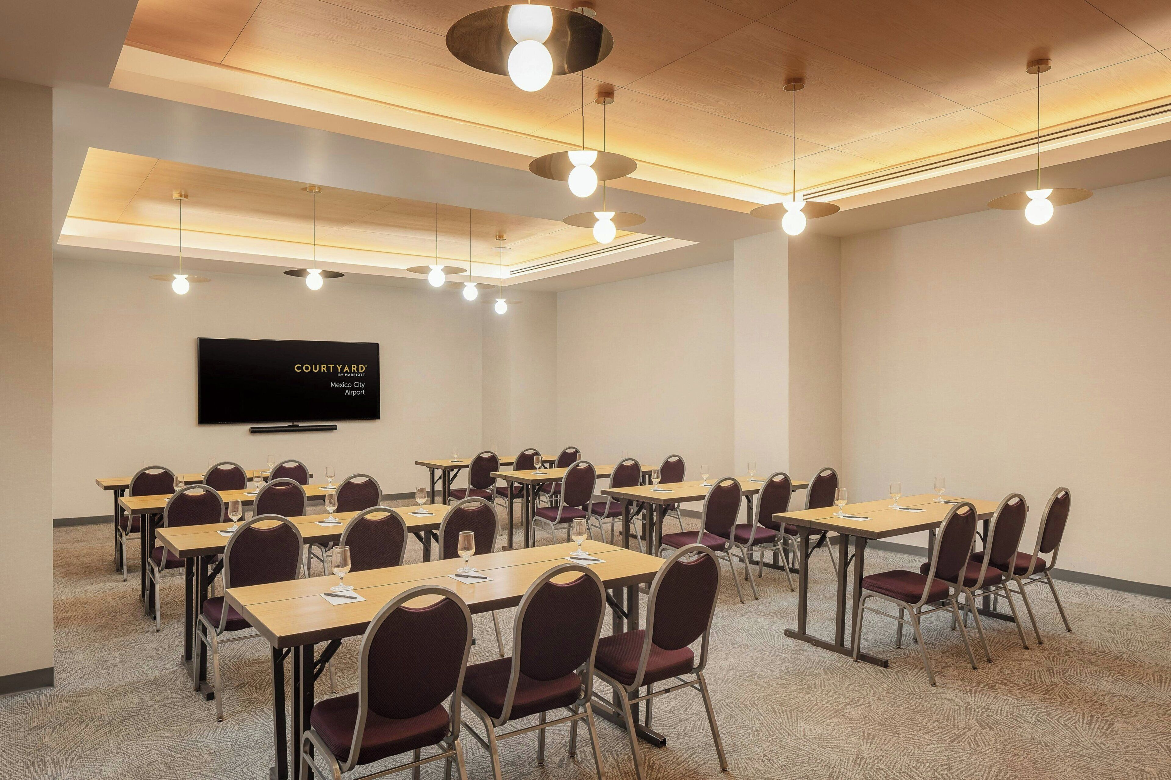 Une salle de conférence équipée de tables, de chaises, d’un téléviseur à écran plat et d’un éclairage au plafond.