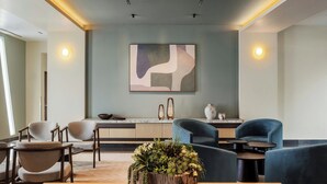 A modern interior with a wooden table, chairs, a plant centerpiece, a kitchen area, and a wall-mounted abstract painting. - Courtyard Mexico City Airport (Mexico City)