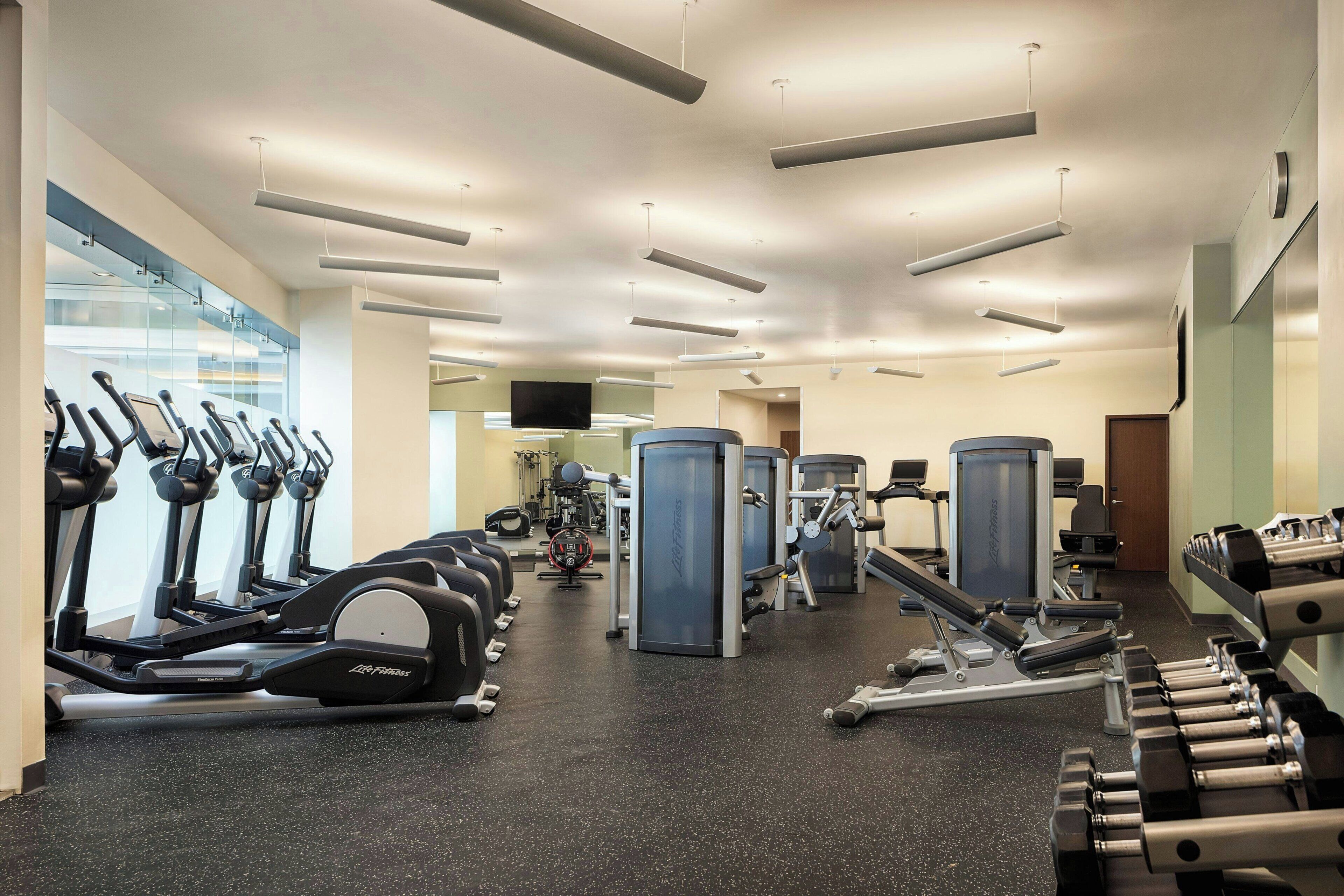 Ein Fitnessstudio mit Laufbändern, Kraftgeräten und einem Fernsehbildschirm.