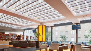 A modern lobby with a high ceiling, a central seating area, a bookshelf, and a large window overlooking the building. - Courtyard Mexico City Airport (Mexico City)