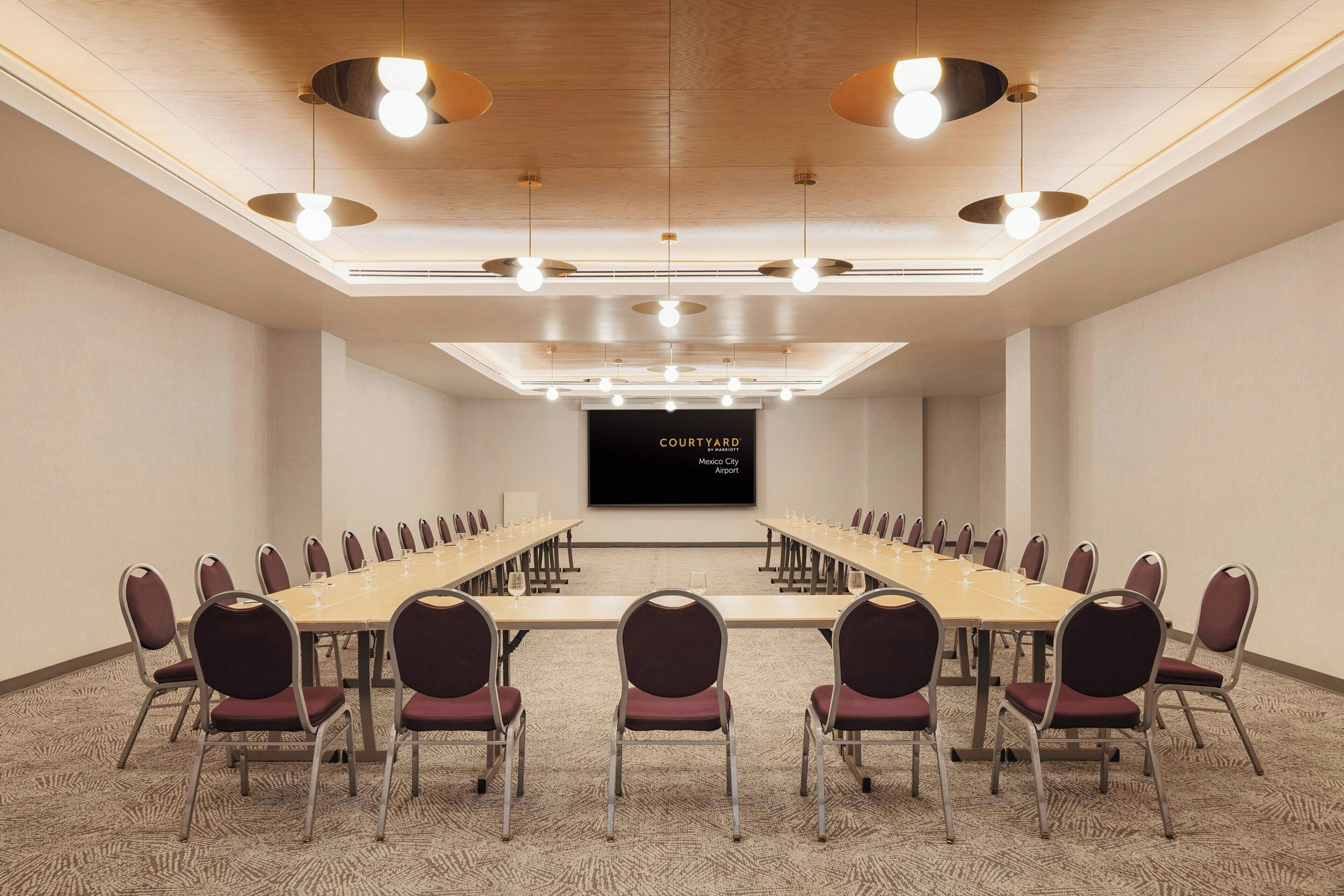 A conference room with a long table, chairs, and a screen displaying 'Courtyard Mexico City Airport.'