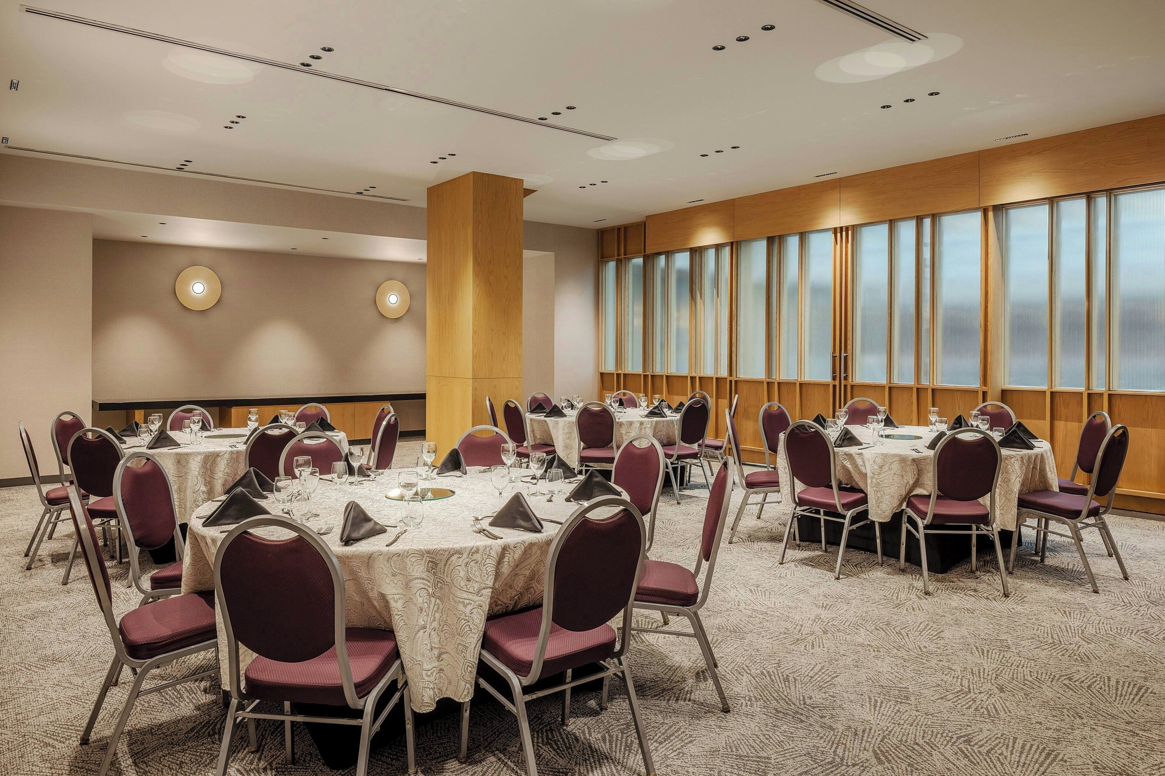 A conference room with round tables, chairs, and a large window with blinds.