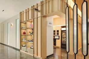 A hotel corridor with a wooden display unit, a sign for the Marriott Bonvoy, and a refrigerated display case.