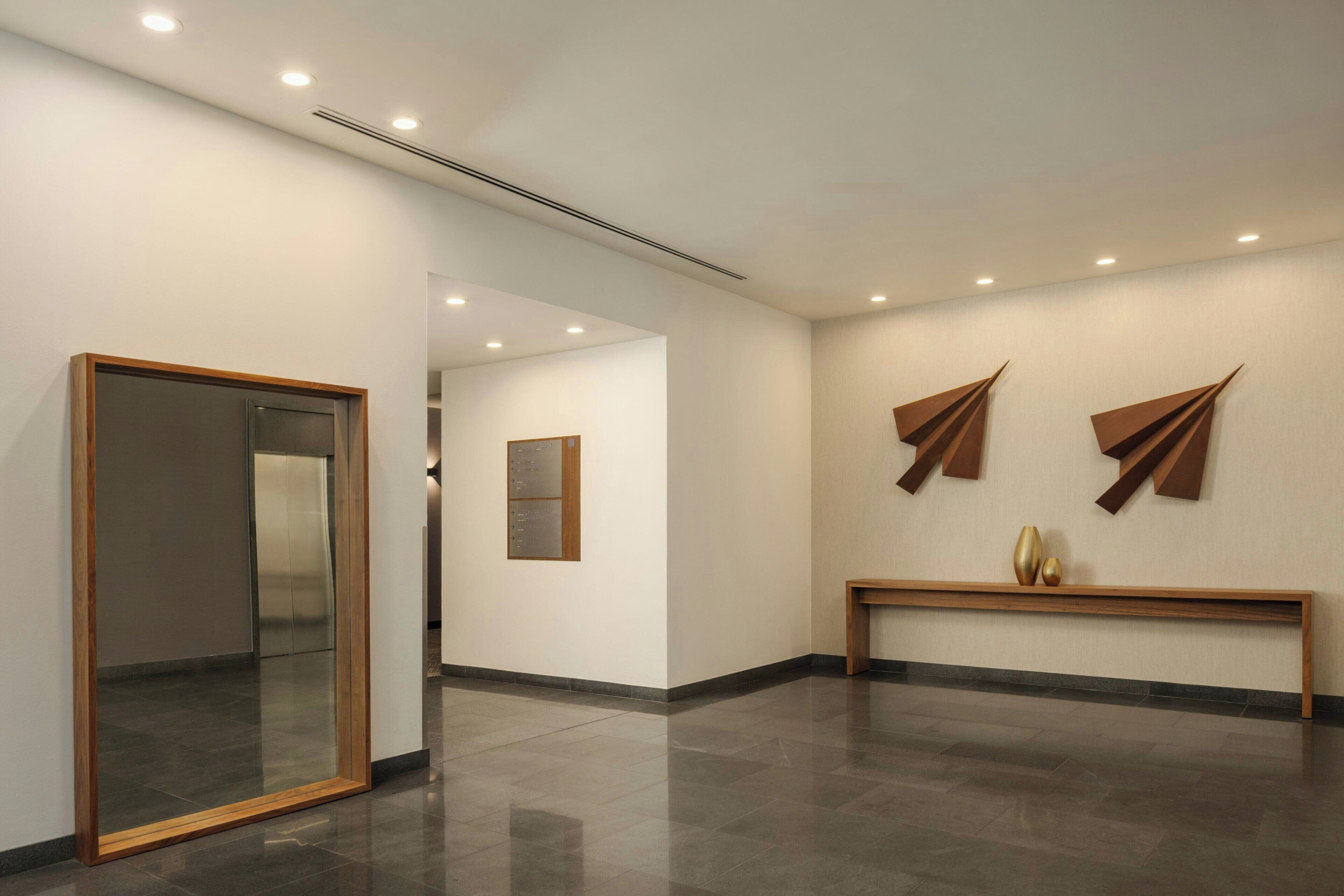 Um corredor com espelho, um banco e arte abstrata nas paredes.