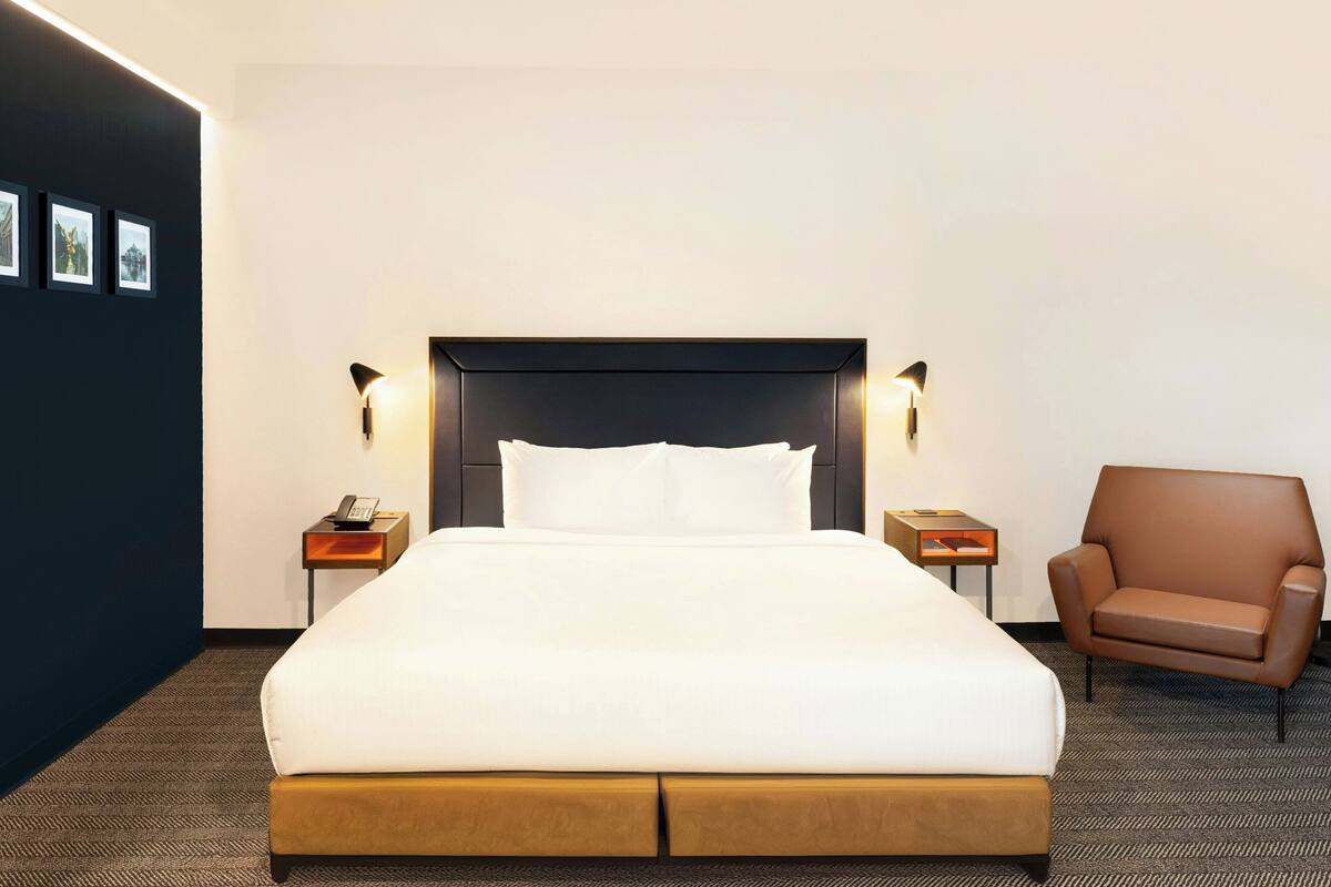 A hotel room with a large bed, two bedside tables, a chair, and framed pictures on the wall.
