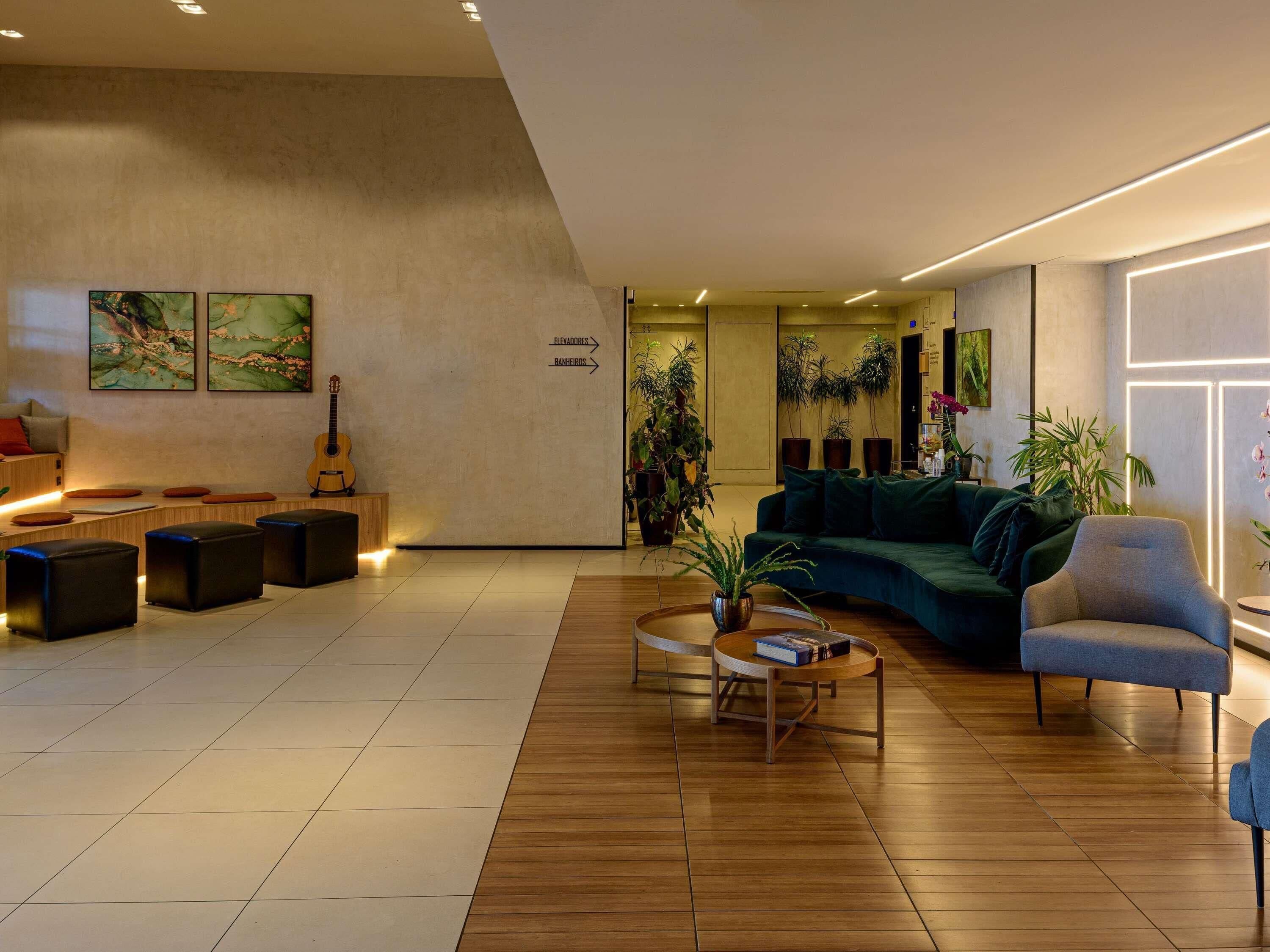 Um hall moderno com piso de madeira, sofá verde, mesa de centro e plantas em vasos.