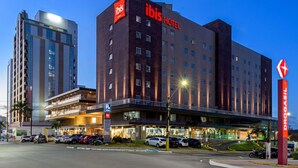Een modern hotel met een opvallend ibis logo, meerdere verdiepingen en een parkeerplaats ervoor.