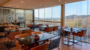 Een modern restaurant met meerdere tafels en stoelen, grote ramen met uitzicht op het platteland.