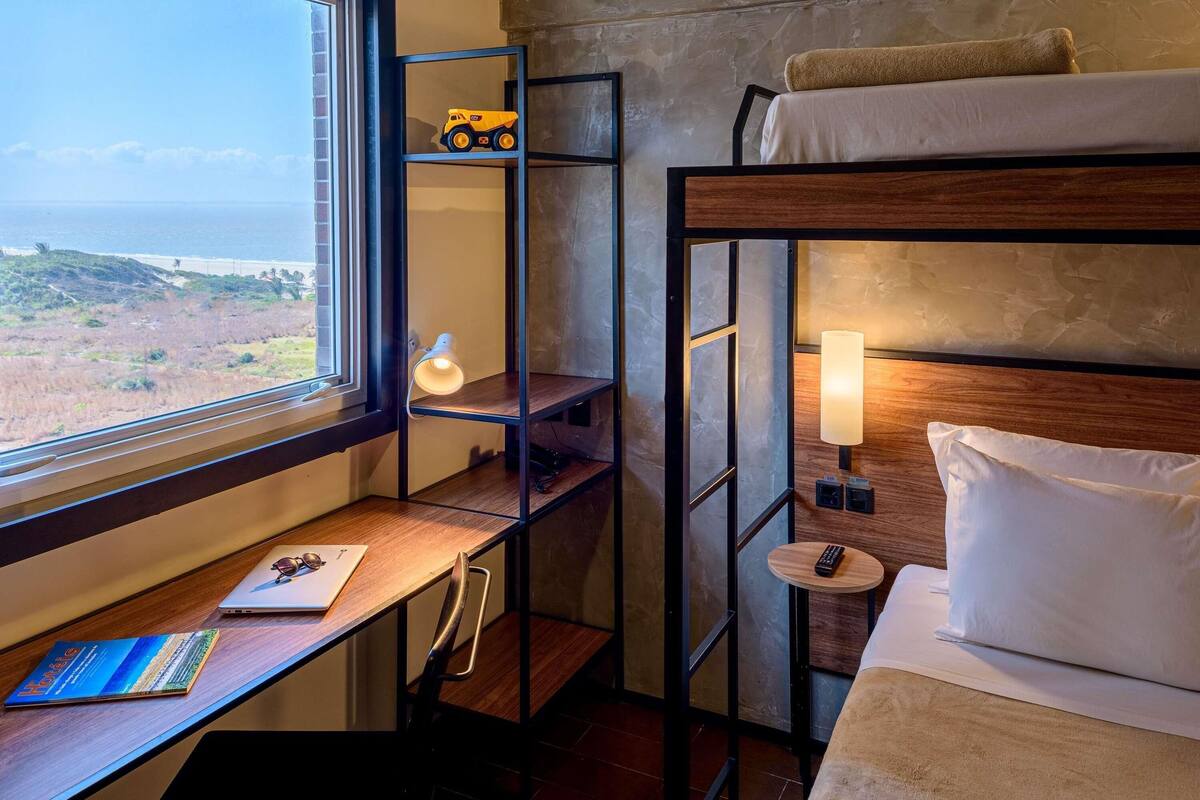 Uma cama de beliche com vista para a paisagem, uma escrivaninha com abajur e uma prateleira com um brinquedo.