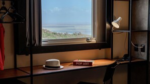 Een kamer met een bureau, een stoel, een raam met uitzicht op het strand, een lamp en een telefoon.