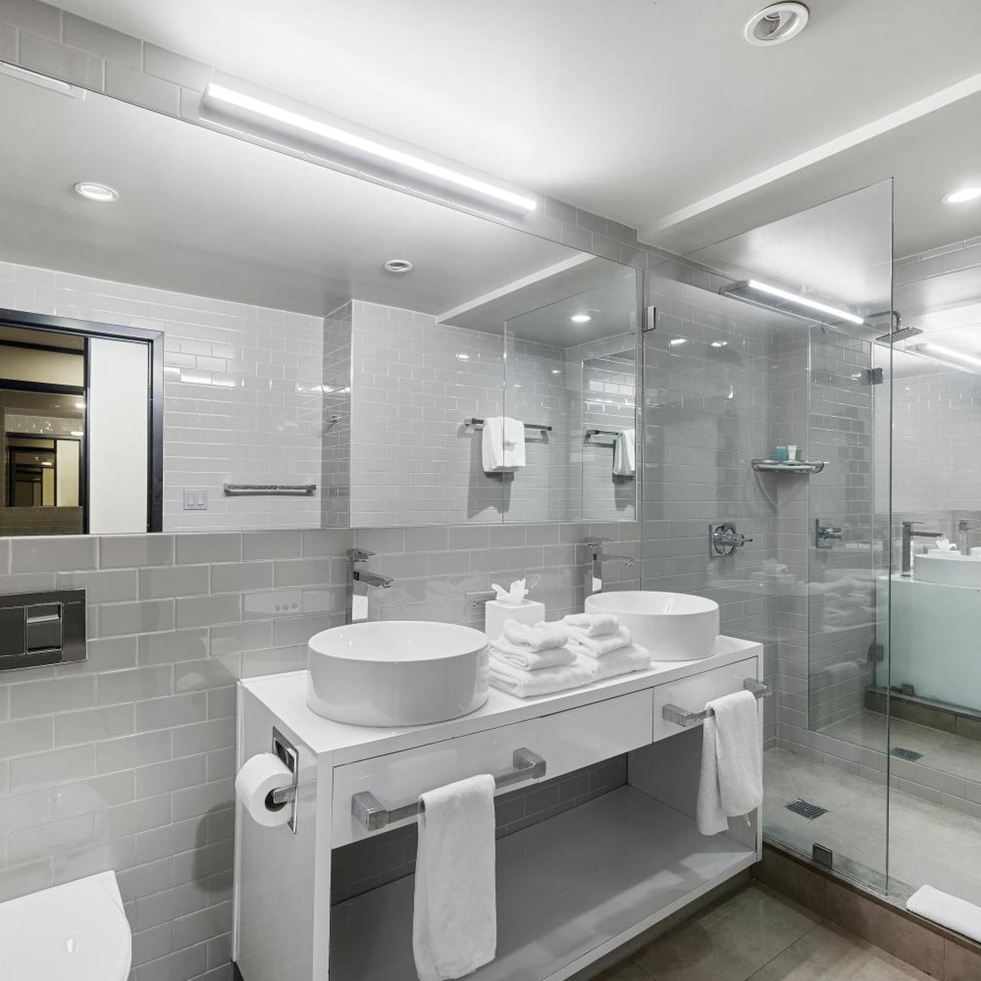 A modern bathroom with two sinks, a glass shower enclosure, and a large mirror.