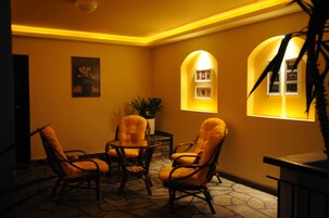 A warmly lit room with four cushioned chairs around a small table, a potted plant, and two illuminated windows.