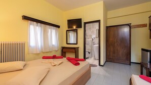 A hotel room with a bed, a wooden wardrobe, a bathroom with a shower, and a television mounted on the wall. - Hotel Petunia (Sithonia)