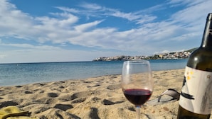 A beach with a wine glass and bottle, a clear sky, and a distant town. - Hotel Petunia (Sithonia)