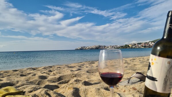 A beach with a wine glass and bottle, a clear sky, and a distant town. - Hotel Petunia (Sithonia)