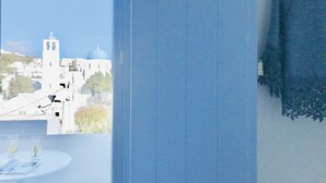 Habitación con vistas a edificios blancos y cúpulas azules, una mesa redonda con vasos, y una cortina azul.
