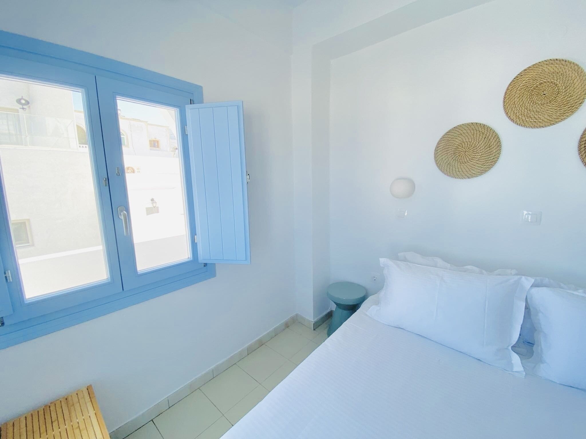 A bedroom with a bed, a window with blue shutters, a toilet, and a wall with woven wall art.