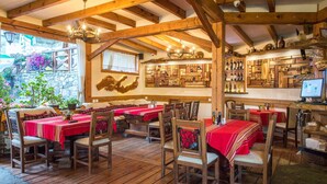 A rustic dining area with wooden beams, red tablecloths, and wooden chairs. - Kamelia (Smolyan)
